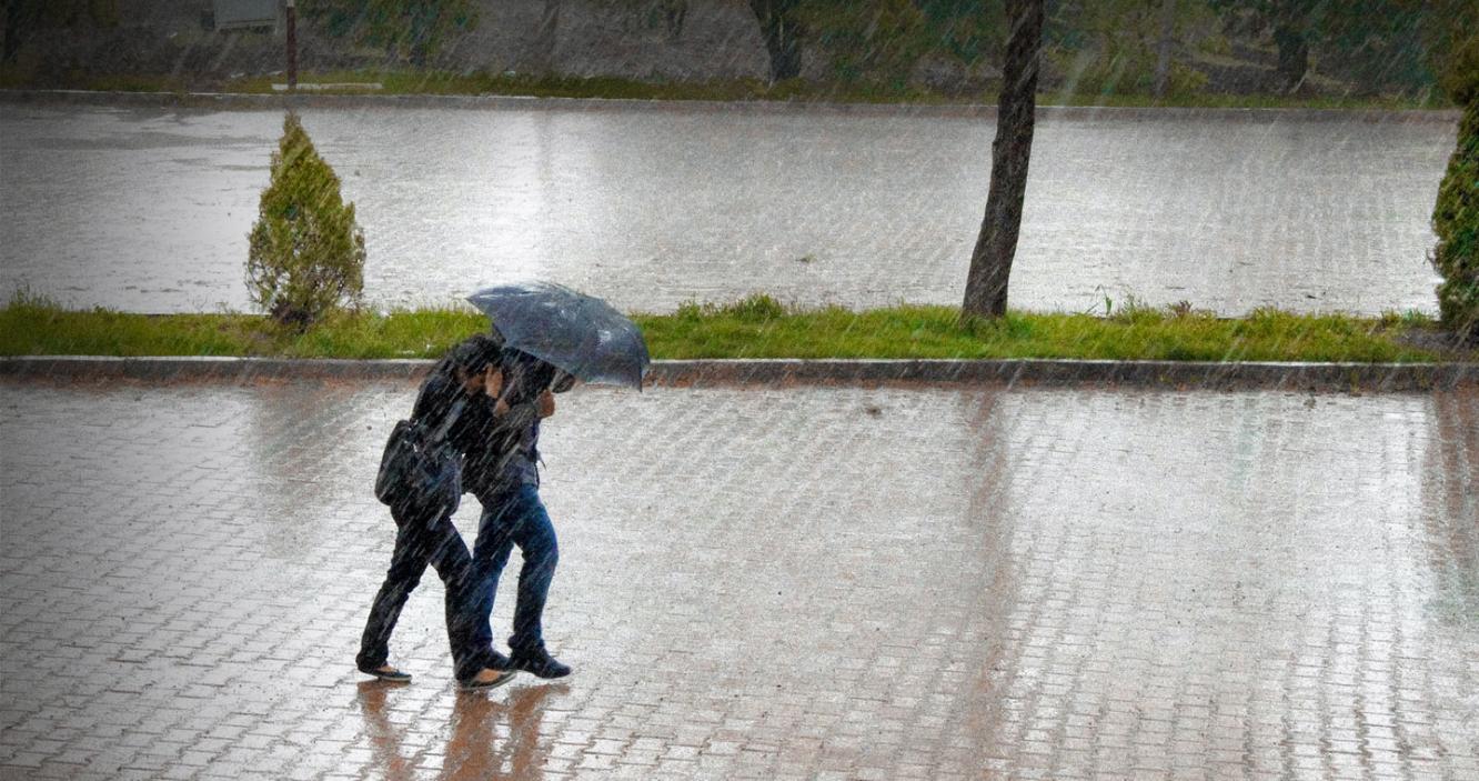 Two people walking in heavy rain, protected by an umbrella