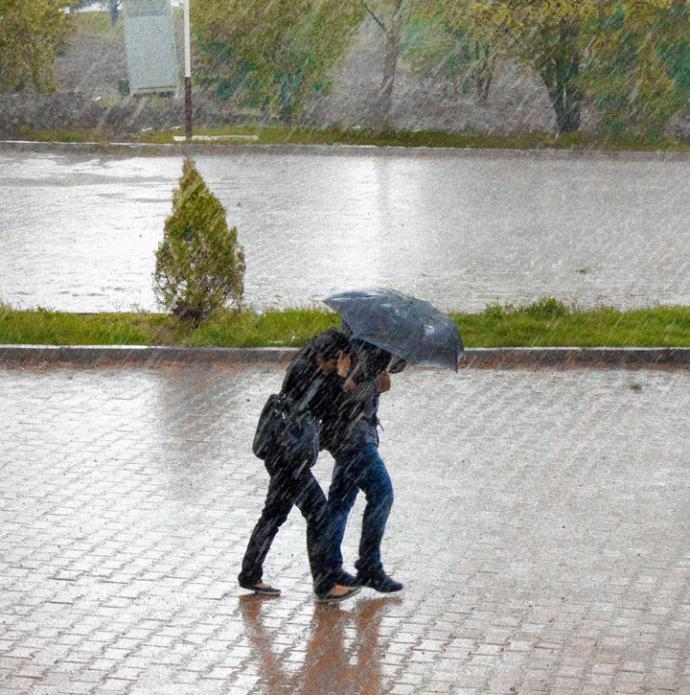 Two people walk through heavy rain, using an umbrella for protection